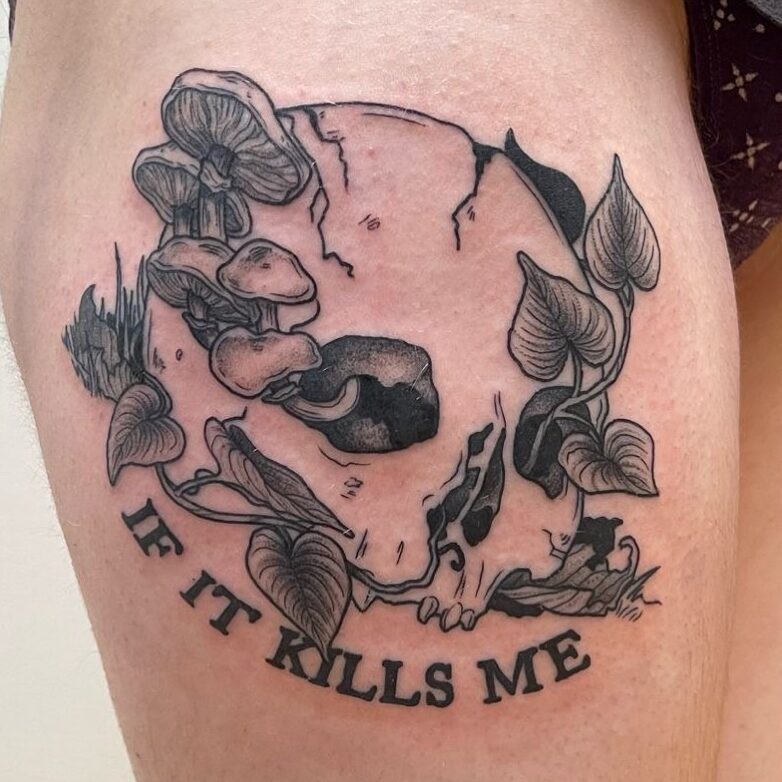 a tattoo of a skull with plants and mushrooms coming out of it, reading "If it kills me"