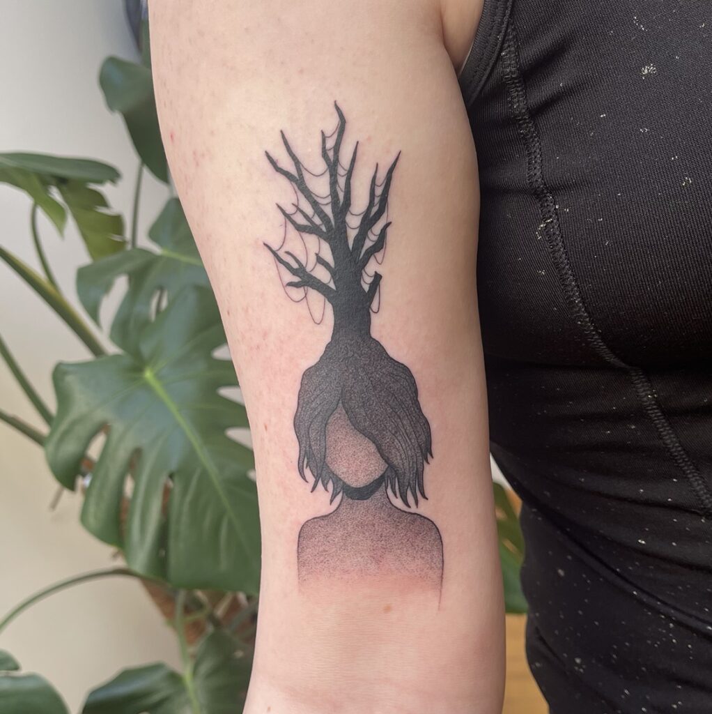 a tattoo of a featureless faced person with a leafless tree growing out of the top of their head