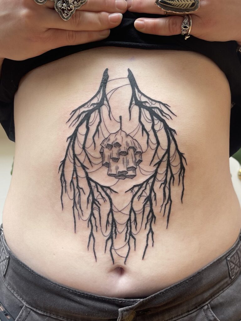 a tattoo of a mostly symmetrical black branches surrounding a paper wasp next with cobwebs hanging off of all of it, placed on the center stomach